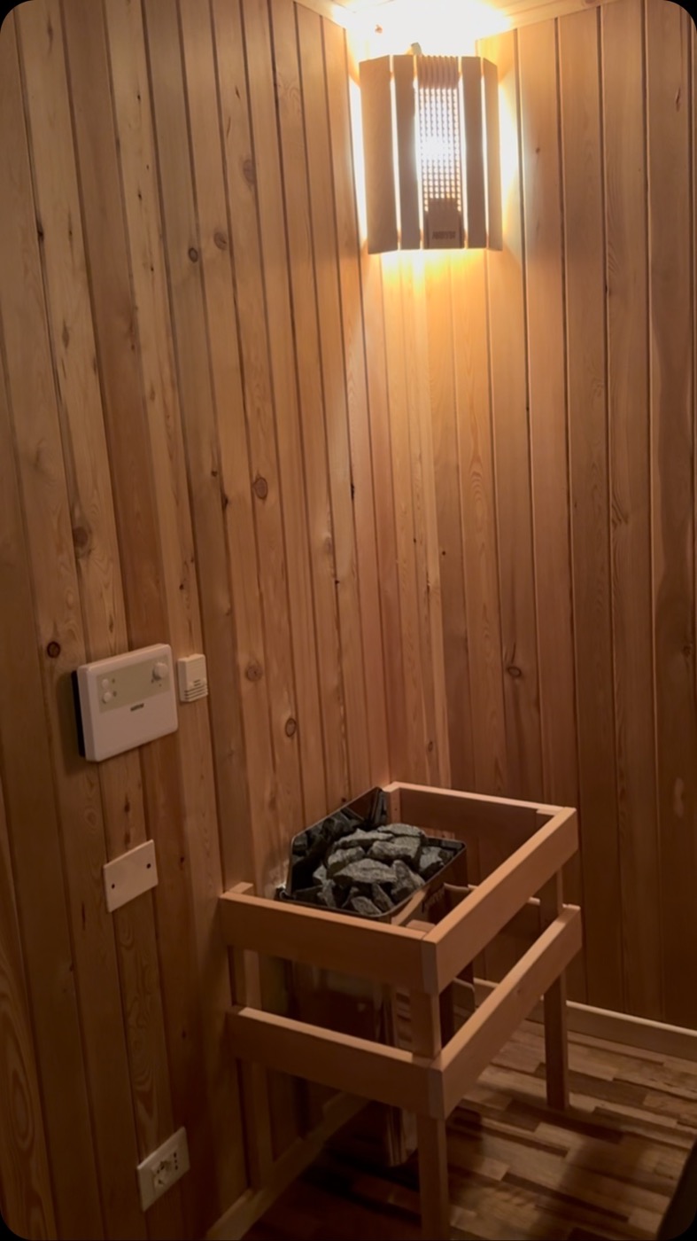 La parete di legno chiaro della biosauna con la stufa a pietre e la lampada